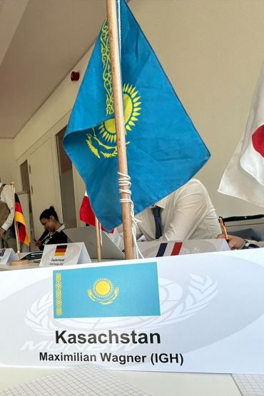 Fotografie: Auf einem Namensschild steht Maximilian Wagners Name als Vertreter Kasachstans, dahinter eine kasachische Flagge.