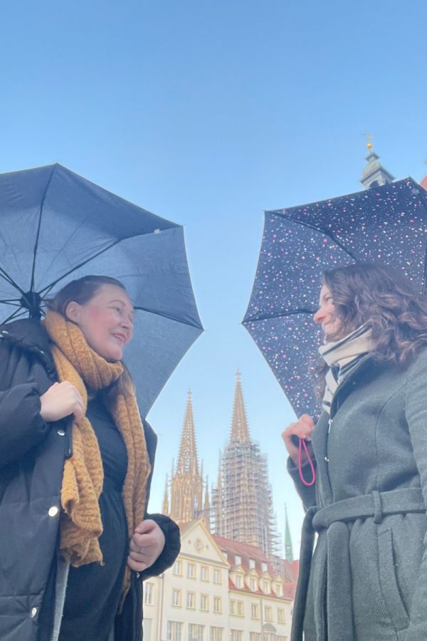 Fotografie- Agnes Gerstenberg und Lisa Hörmann mit aufgespannten Regenschirmen mit Dom im Hintergrund