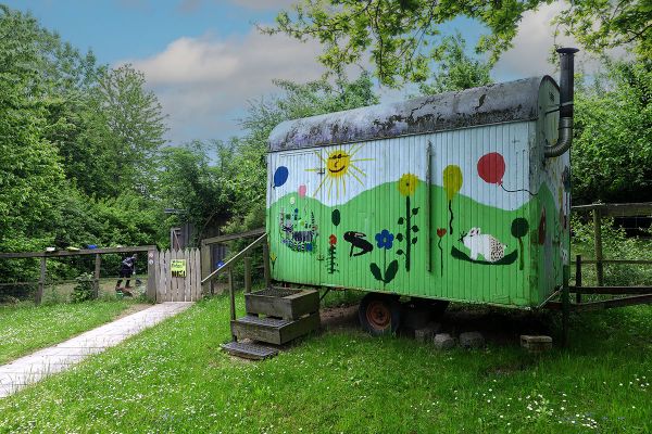 Das Bild zeigt einen bunt bemalten Bauwagen auf einer Wiese. 