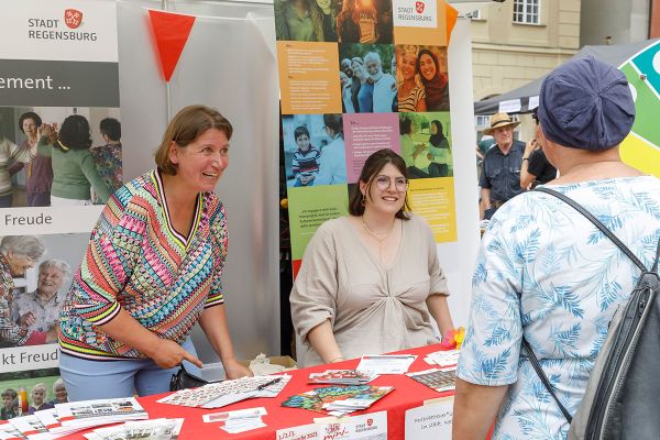 Zwei Personen beraten jemanden an einem Infostand
