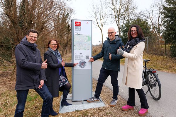 Fotografie - Auf dem Foto stehen (v.l.n.r.) Nahmobilitätskoordinator Thomas Großmüller, Oberbürgermeisterin Gertrud Maltz-Schwarzfischer, Referatsleiter Planungs- und Baureferat Florian Plajer und Amtsleiterin Stadtplanungsamt Tanja Flemmig vor einer Steele der Radlroute 05 mit dem Aufkleber für den Deutschen Fahrradpreis 2025 TOP-Projekt Infrastruktur.