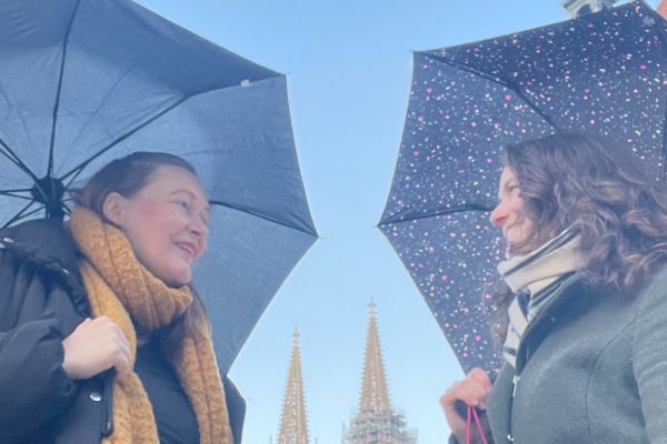 Fotografie- Agnes Gerstenberg und Lisa Hörmann mit aufgespannten Regenschirmen mit Dom im Hintergrund