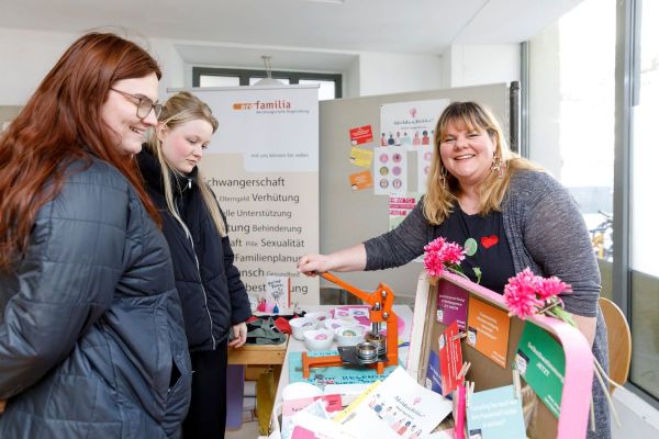 Fotografie - Stand des AK Mädchen* mit Ansprechperson Micha Schindler und Stand von pro familia im Regensburg mit Besucherinnen 