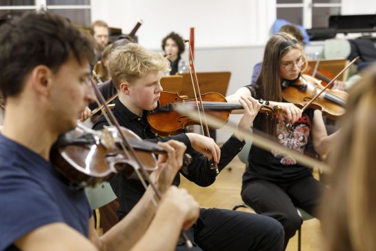 Fotografie: Drei Jugendliche spielen Geige im Orchester