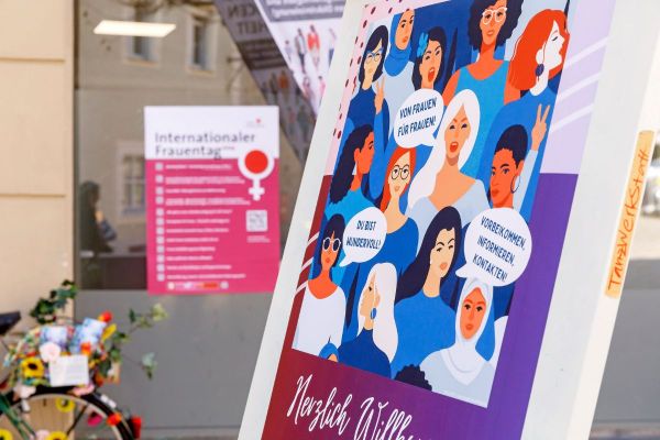 Fotografie - Plakat „Herzlich Willkommen zur Frauenmesse“ vor dem Raum für Engagement, im Hintergrund das Plakat mit den Veranstaltungen zum Internationalen Frauentag. 