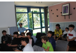 Das Bild wurde in einem Innenraum aufgenommen. Im Hintergrund sieht man ein Fenster. Im Vordergrund sind einige Kinder zu sehen, die gebannt nach links vorne gucken, wo sich der Fernseher befindet, auf dem gerade das Playstation-Spiel Fifa gespielt wird.